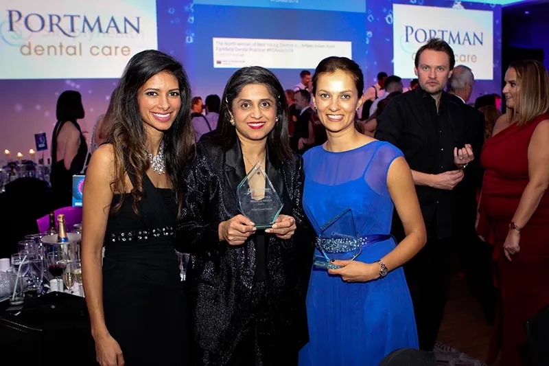 Dr Shabnam and Dr Nikita of West House Dental standing with Dr Shivani Patel of Elleven Dental at the Private Dentistry Awards 2018. They are smiling and holding two glass trophies in a formal ballroom setting with Portman Dental Care branding in the background.